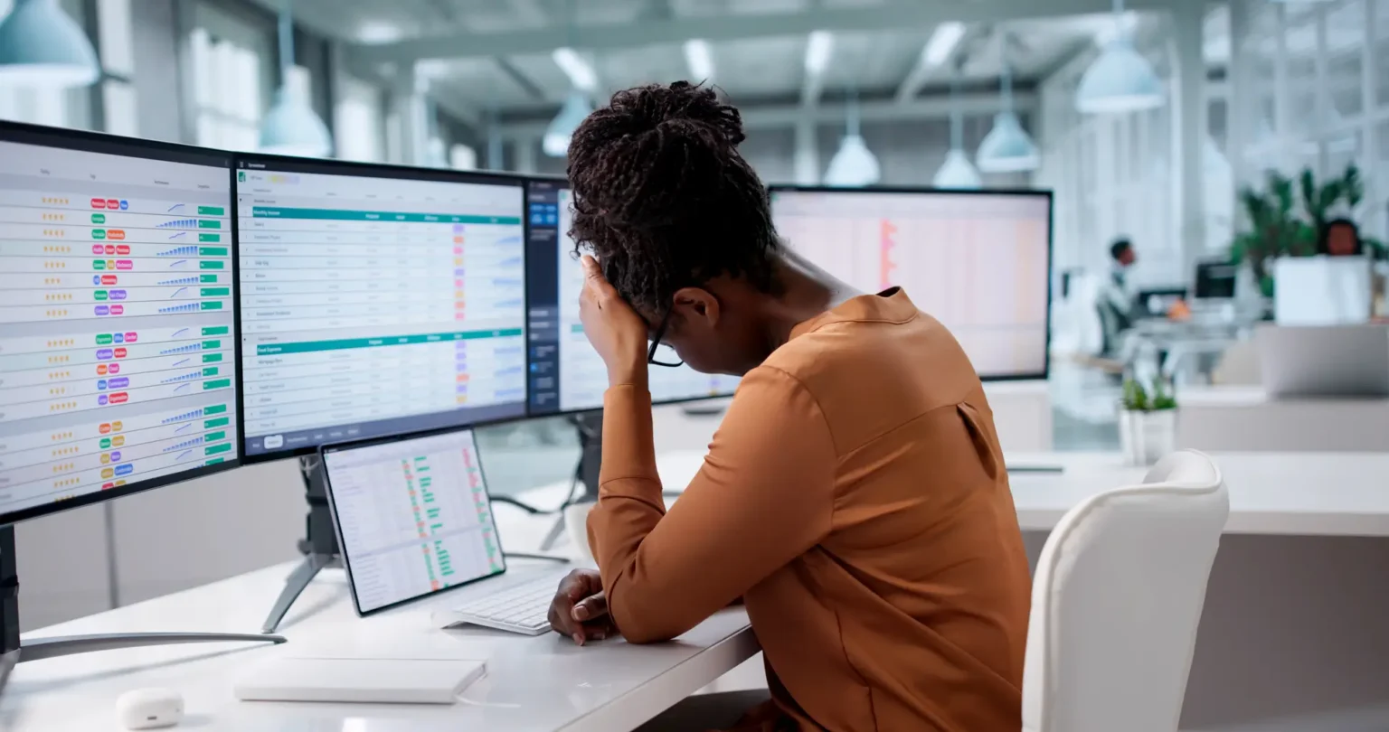 medical professional sits at a workstation with several large monitors displaying data tables charts and analytics dashboards