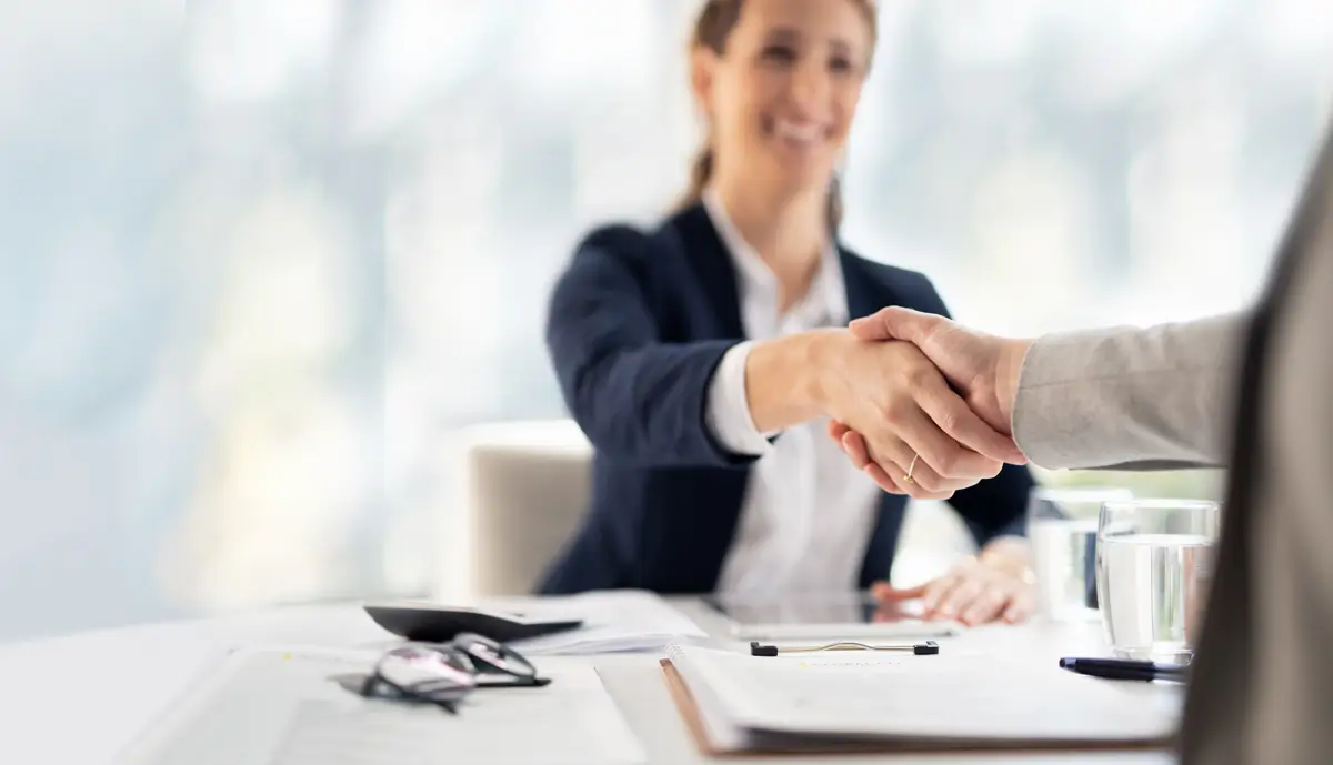 A businesswoman and another person shaking hands in a professional setting, symbolizing agreement or partnership.