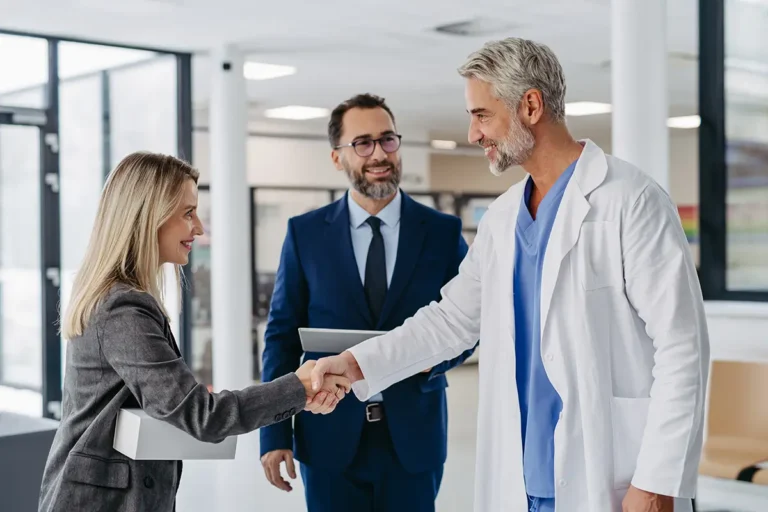 A doctor and business woman engaged in a handshake inside a medical facility.