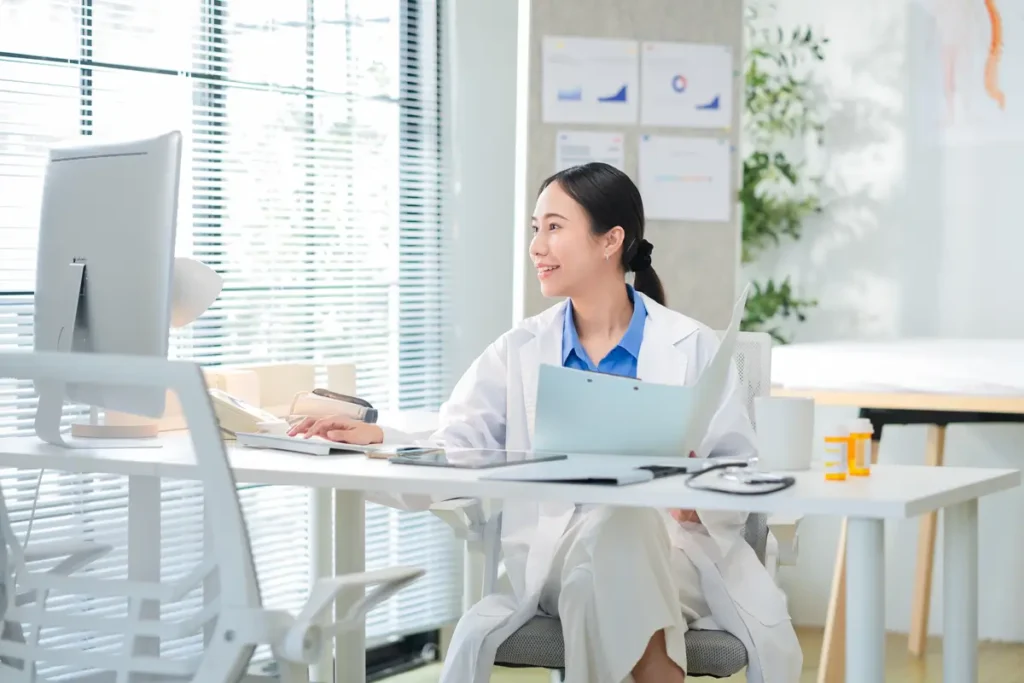 Portrait of a female doctor smiling while working at he r desk in a clinic typing on her laptop and reviewing medical reports